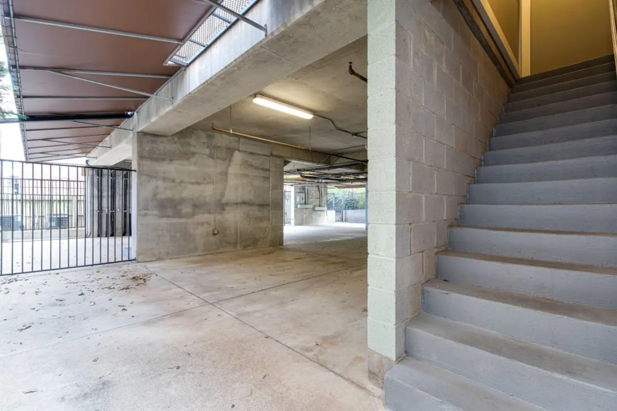 A concrete-walled interior garage space with clear sightlines to a modern staircase and functional lighting fixtures. The area is clean and uncluttered, highlighting its utilitarian purpose and secure environment. The presence of the staircase suggests direct access to living spaces from the garage.
