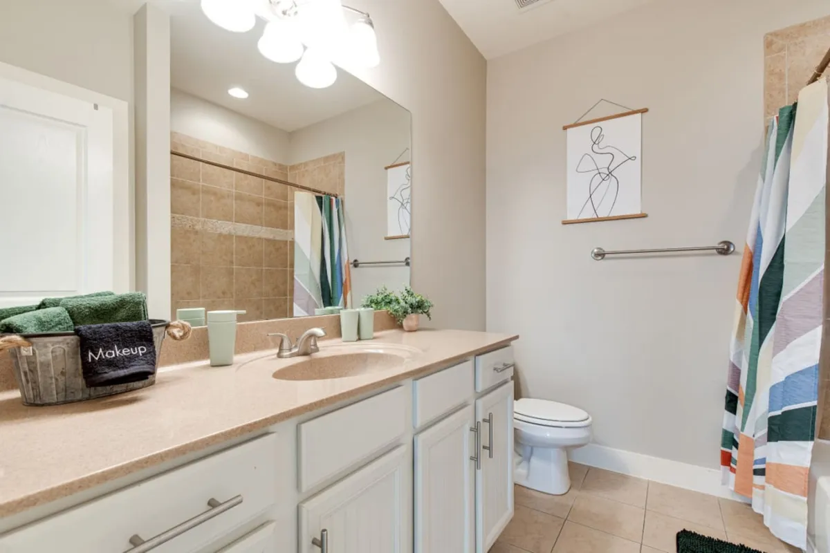 A fresh, calm bathroom scene featuring a vanity with a large mirror, colorful towels, and artwork on the wall. The space is well-lit and designed for relaxation and self-care routines.