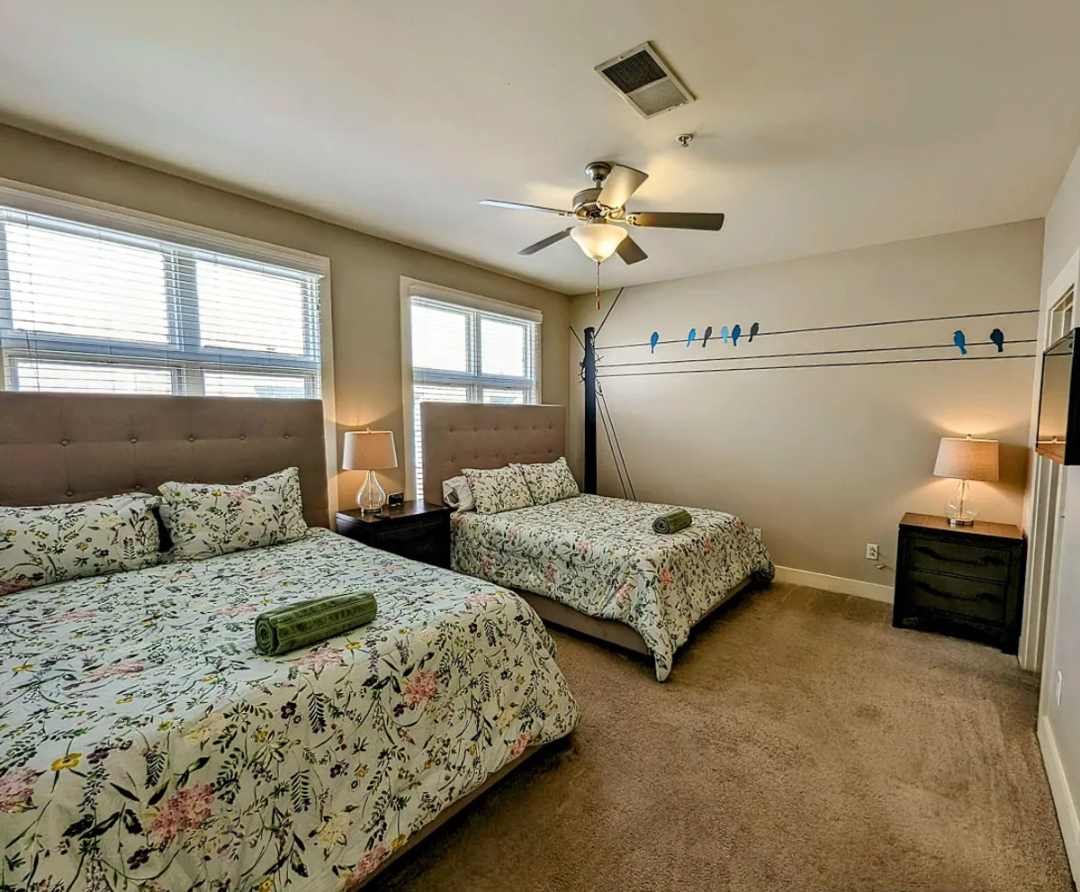 This image features a second-floor bedroom setup with two beds adorned in floral bedding, complemented by decorative bird wall art and functional nightstands with lamps. The arrangement conveys a sense of flexibility—accommodating families or groups—and a cozy, inviting atmosphere ideal for restful nights or quiet reading.