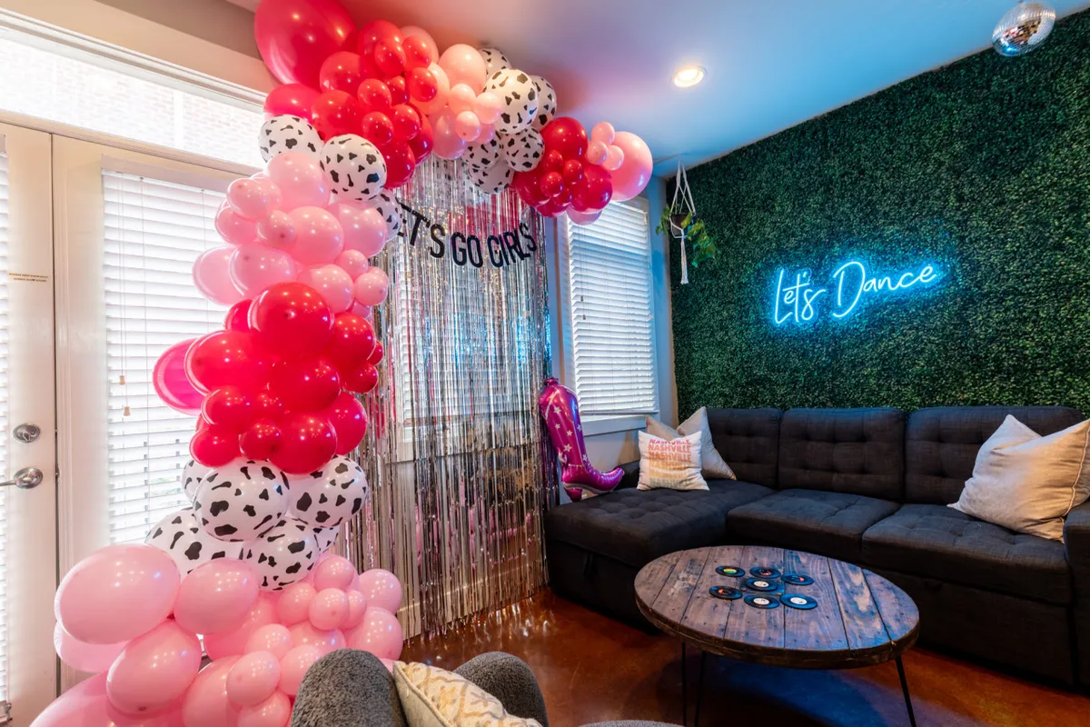 The image showcases a vibrant Nashville condo living room with a colorful balloon archway, a glowing neon sign, stylish seating, and lush decorative plants, creating the perfect backdrop for festive gatherings and memorable celebrations.